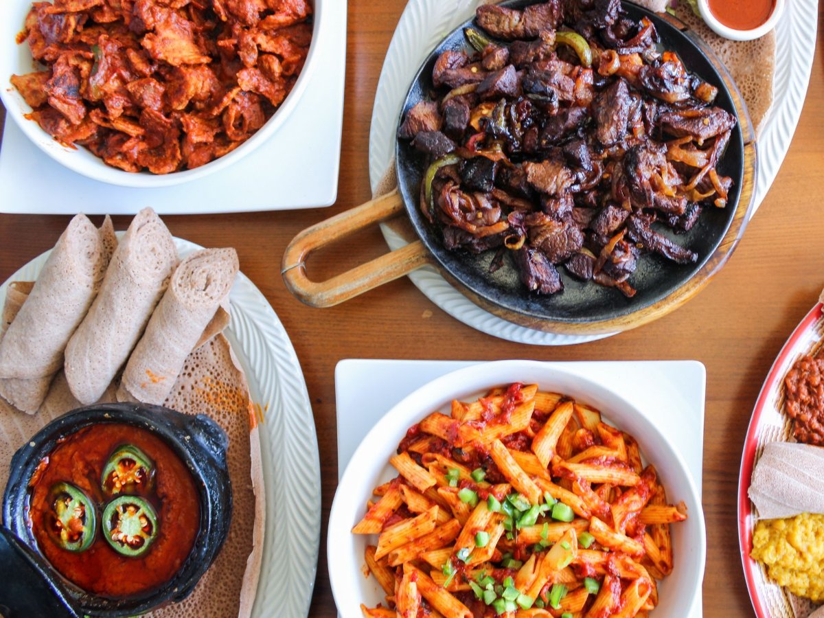 Table spread of Eritrean and Ethiopian dishes at Banna Restaurant in Dallas: sizzling beef tibs, tibs firfir, pasta and combination platters on injera